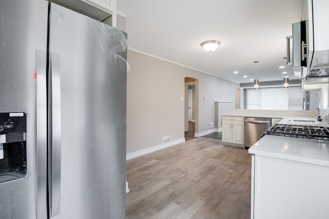 kitchen with decorative light fixtures, light stone countertops, stainless steel appliances, sink, and light wood-type flooring