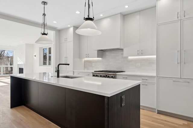 kitchen featuring a kitchen island with sink, sink, and hanging light fixtures