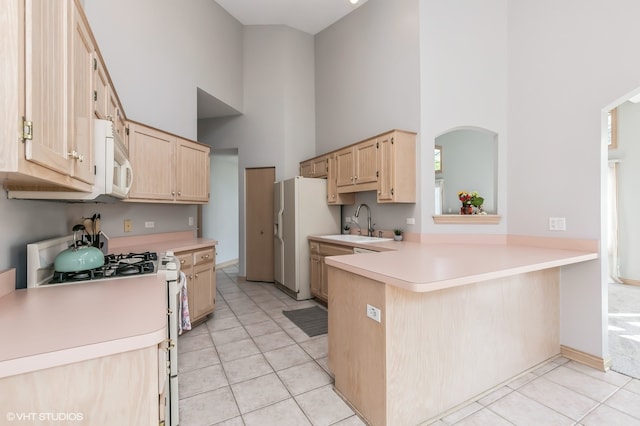 kitchen with white appliances, light brown cabinetry, kitchen peninsula, and a high ceiling