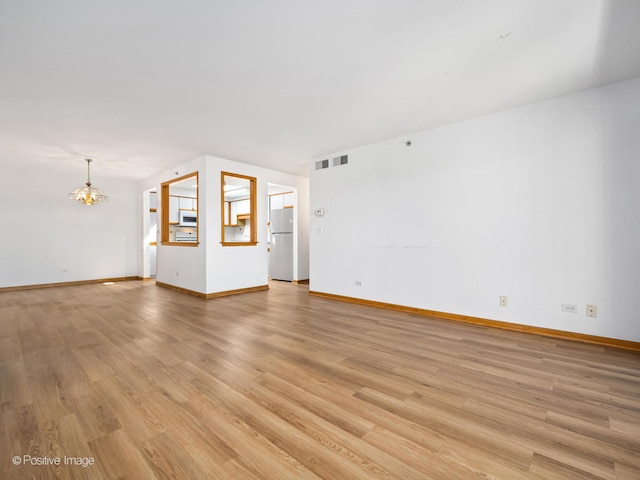 unfurnished living room featuring a chandelier and light hardwood / wood-style flooring