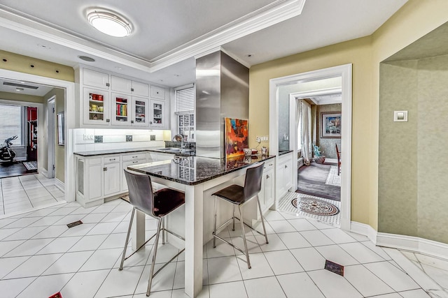 kitchen featuring a breakfast bar area, ornamental molding, sink, white cabinetry, and dark stone countertops