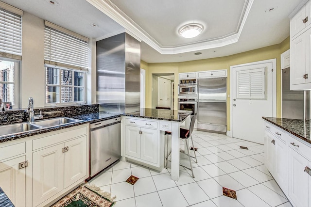 kitchen featuring white cabinets, dark stone countertops, sink, built in appliances, and ornamental molding