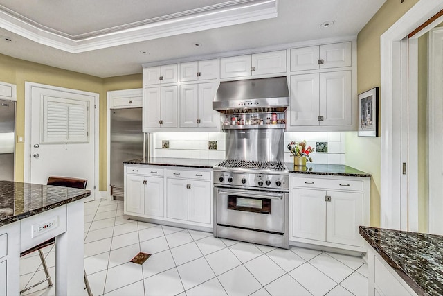 kitchen with high end appliances, wall chimney exhaust hood, white cabinetry, and backsplash