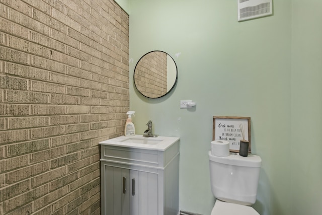 bathroom featuring brick wall, toilet, and vanity