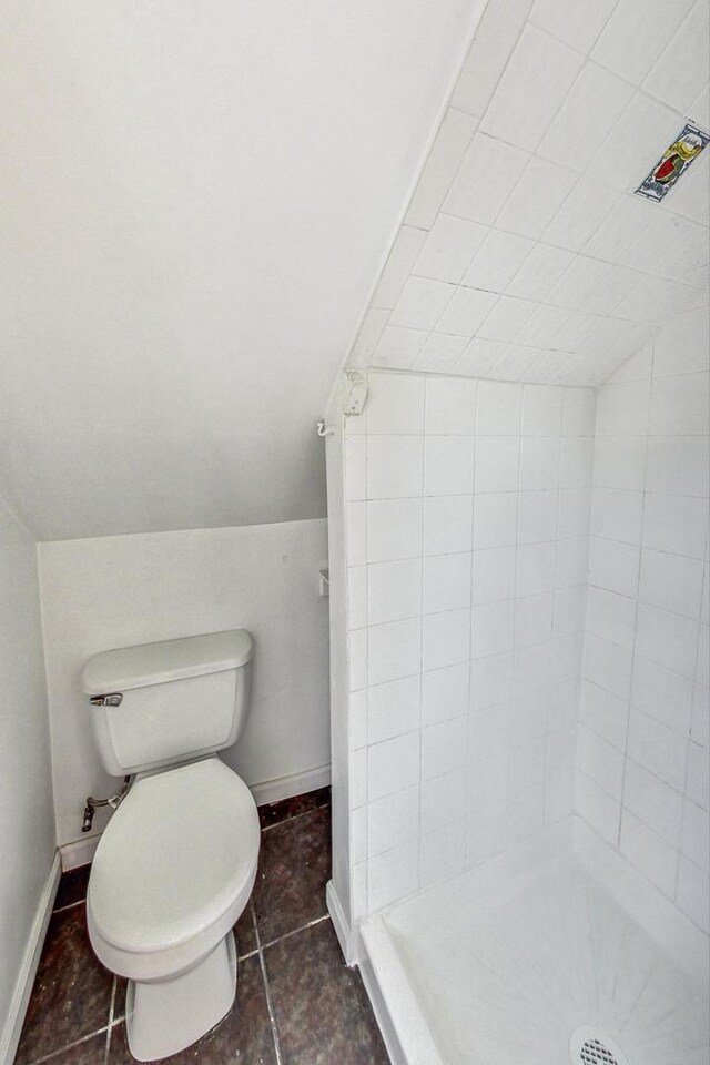 full bath featuring tile patterned floors, toilet, a stall shower, baseboards, and lofted ceiling