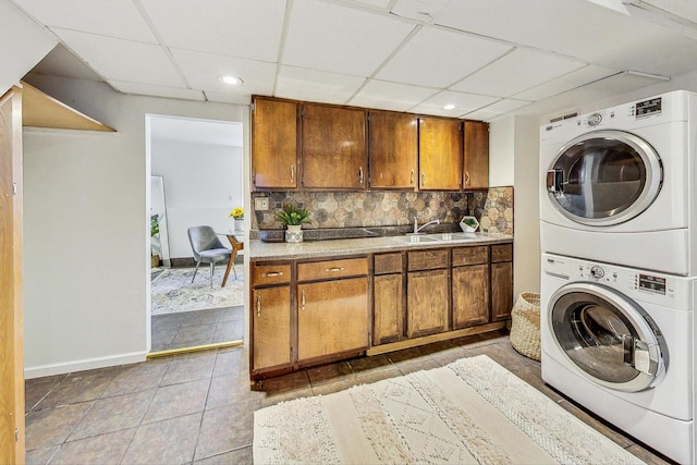 laundry area with a sink, baseboards, stacked washer / dryer, tile patterned flooring, and laundry area