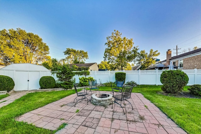 view of patio / terrace featuring fence, a fire pit, a storage unit, and an outbuilding