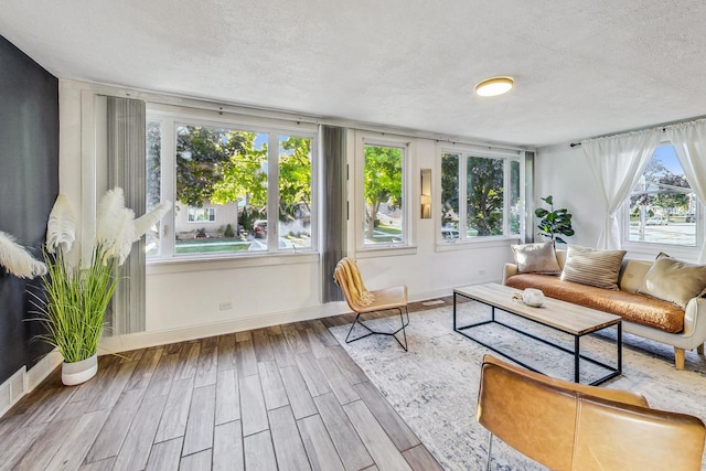 sunroom with wood finished floors, a textured ceiling, and baseboards