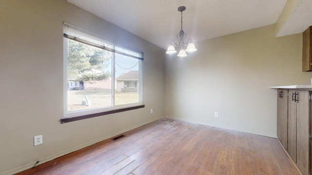 unfurnished dining area featuring hardwood / wood-style flooring, a healthy amount of sunlight, and a notable chandelier