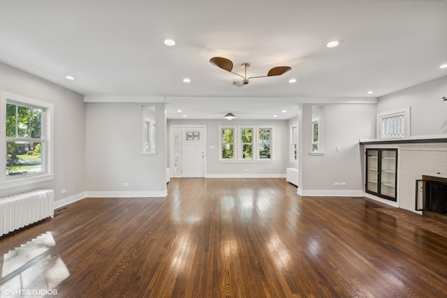 unfurnished living room with a fireplace, dark hardwood / wood-style flooring, radiator heating unit, and ceiling fan