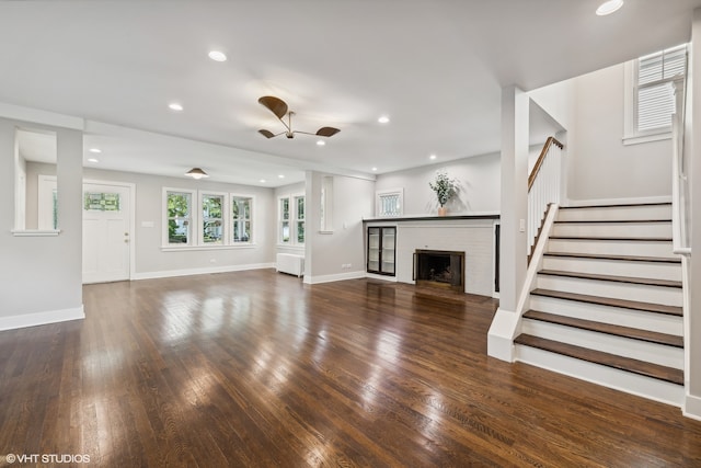 unfurnished living room with a brick fireplace, dark hardwood / wood-style floors, and ceiling fan