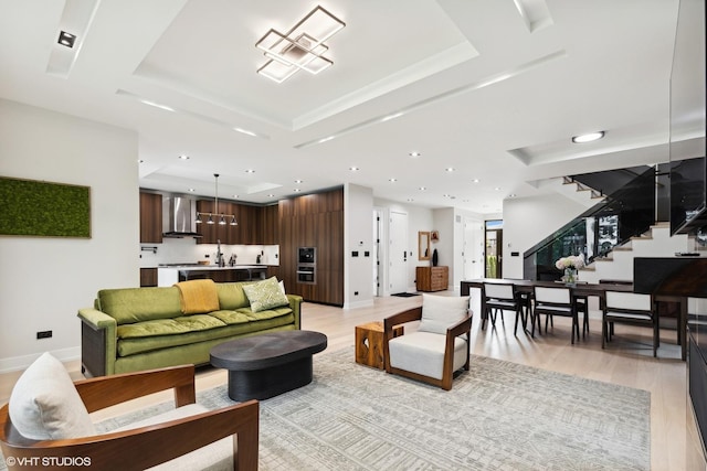 living area with light wood-type flooring, recessed lighting, stairway, baseboards, and a raised ceiling
