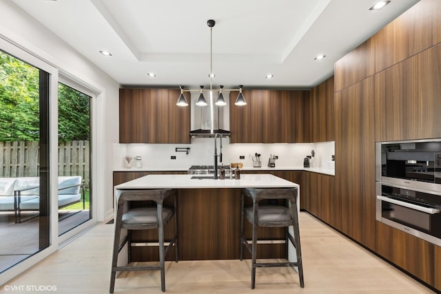 kitchen featuring modern cabinets, a tray ceiling, light wood-style floors, a breakfast bar area, and light countertops
