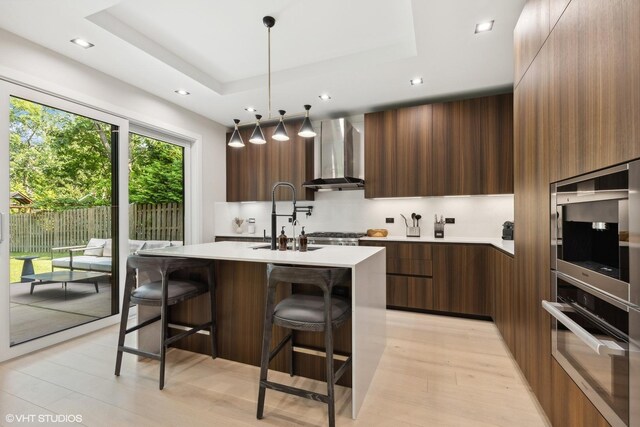 kitchen featuring stainless steel appliances, sink, wall chimney range hood, a breakfast bar area, and a kitchen island with sink