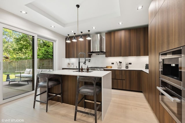 kitchen with modern cabinets, a sink, wall chimney range hood, stainless steel oven, and a raised ceiling