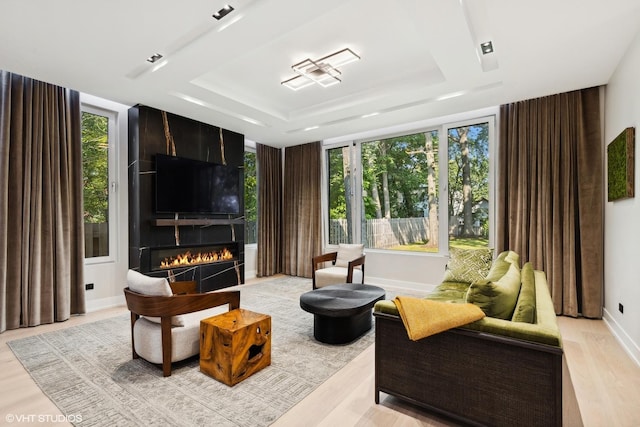 living room featuring a raised ceiling, light wood-style floors, baseboards, and a large fireplace