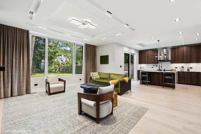 living room with plenty of natural light, recessed lighting, a raised ceiling, and light wood-style floors