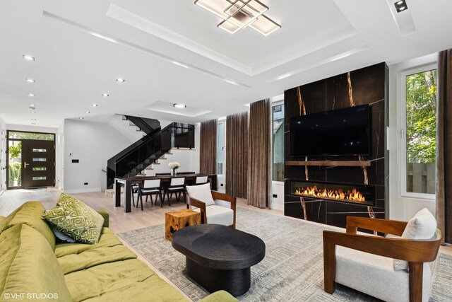 living room featuring plenty of natural light, a raised ceiling, light wood-type flooring, and a fireplace