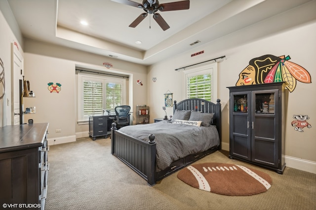 carpeted bedroom with multiple windows, a raised ceiling, and ceiling fan