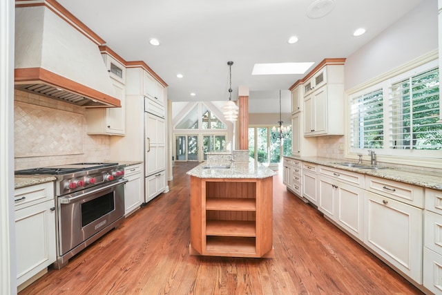 kitchen featuring premium range, hanging light fixtures, a kitchen island with sink, light stone countertops, and custom range hood