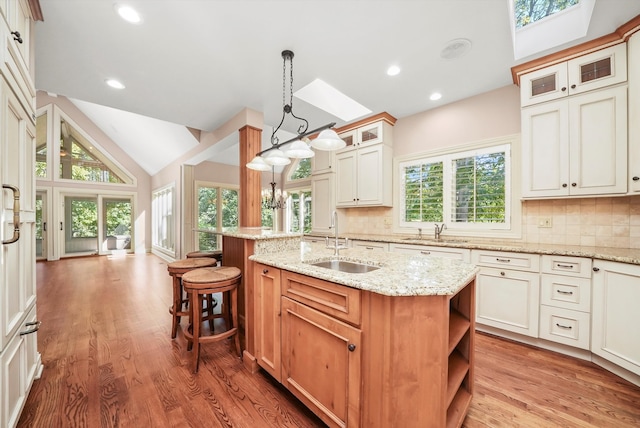 kitchen featuring vaulted ceiling, decorative light fixtures, sink, a kitchen island with sink, and light stone countertops