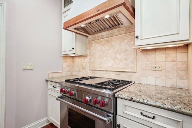 kitchen featuring high end stainless steel range oven, premium range hood, light stone countertops, white cabinets, and decorative backsplash