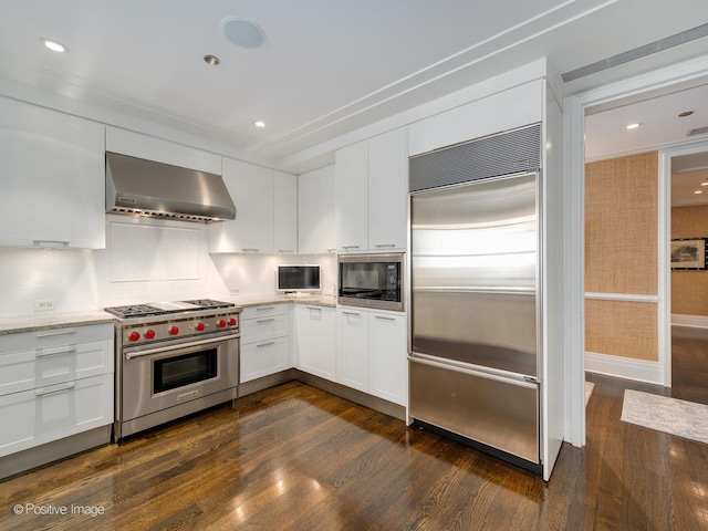 kitchen with dark wood-type flooring, built in appliances, white cabinets, wall chimney range hood, and light stone countertops