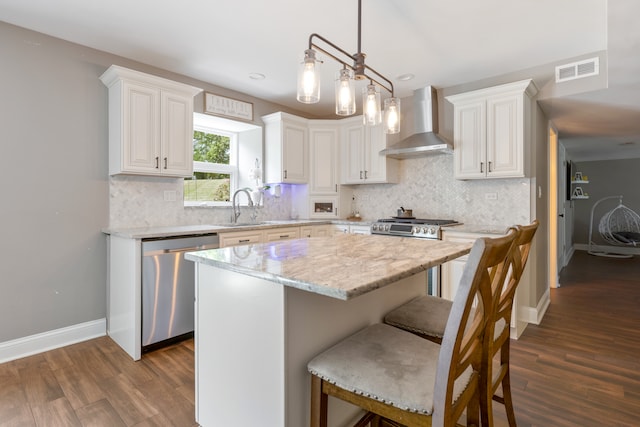 kitchen with hanging light fixtures, white cabinets, wall chimney exhaust hood, a center island, and stainless steel dishwasher