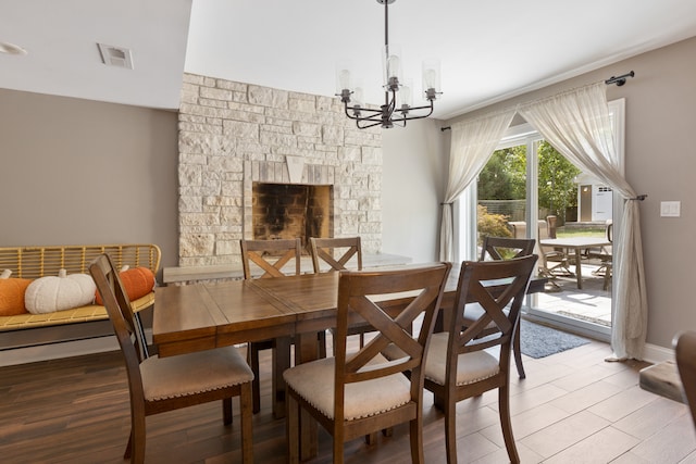 dining area with an inviting chandelier, hardwood / wood-style flooring, and a stone fireplace