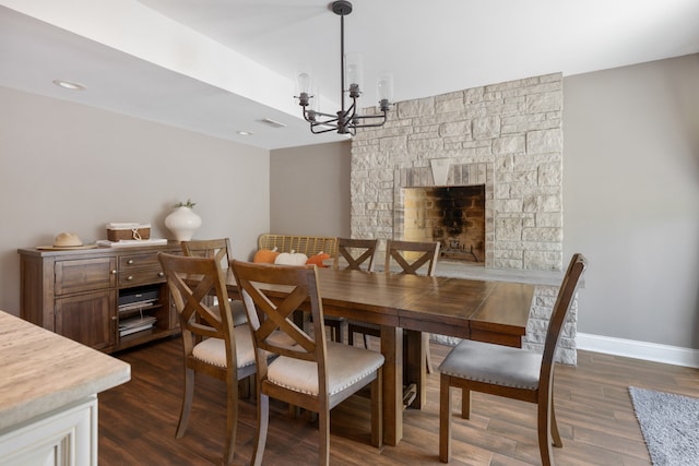 dining space featuring a stone fireplace, a chandelier, and dark hardwood / wood-style flooring