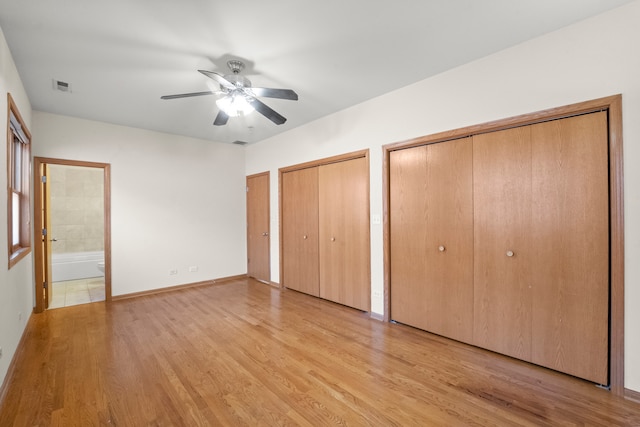 unfurnished bedroom featuring ceiling fan, light hardwood / wood-style flooring, ensuite bathroom, and multiple closets