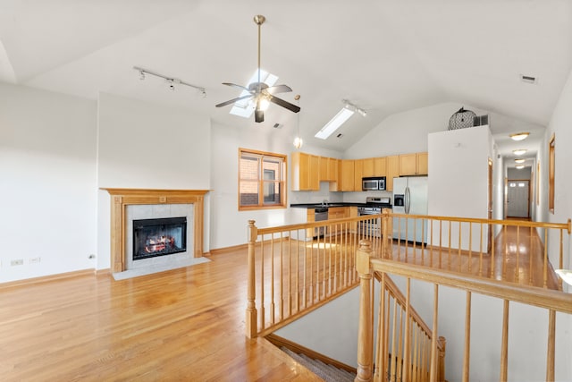 interior space featuring ceiling fan, light hardwood / wood-style flooring, track lighting, high vaulted ceiling, and a fireplace