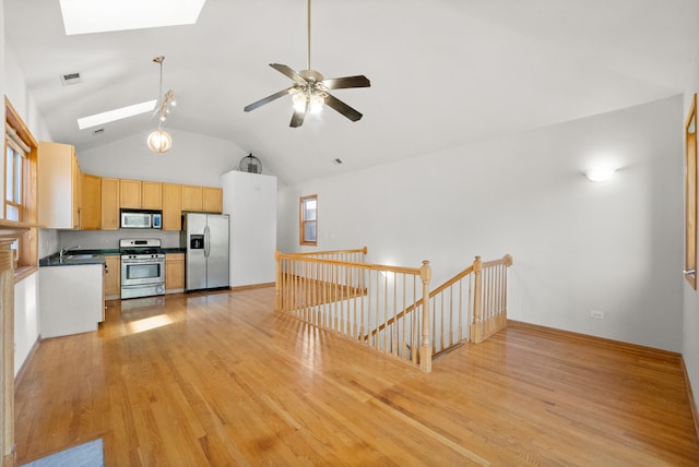 kitchen with light brown cabinets, stainless steel appliances, lofted ceiling with skylight, ceiling fan, and light hardwood / wood-style flooring