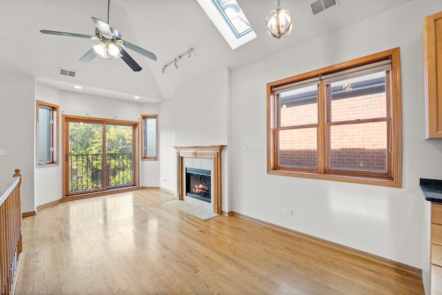 unfurnished living room featuring ceiling fan with notable chandelier, lofted ceiling with skylight, a tiled fireplace, and plenty of natural light