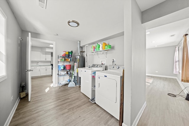 washroom with gas water heater, washer and clothes dryer, and light hardwood / wood-style flooring