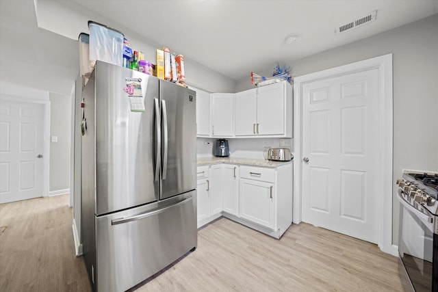 kitchen with light wood-type flooring, light stone counters, stainless steel appliances, and white cabinetry