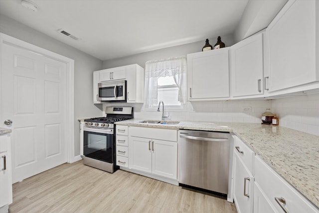 kitchen with light hardwood / wood-style flooring, appliances with stainless steel finishes, light stone counters, white cabinetry, and sink