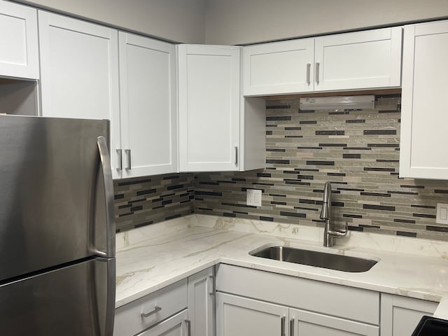 kitchen with tasteful backsplash, stainless steel refrigerator, sink, light stone counters, and white cabinets