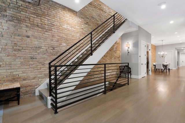 stairway with hardwood / wood-style floors, a towering ceiling, an inviting chandelier, and brick wall