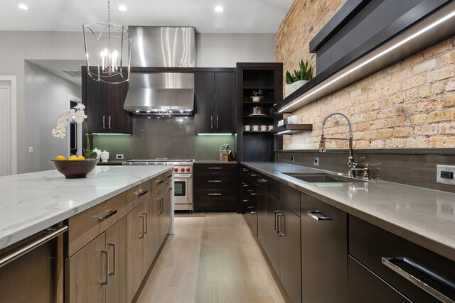 kitchen featuring pendant lighting, sink, wall chimney range hood, premium range, and light hardwood / wood-style floors