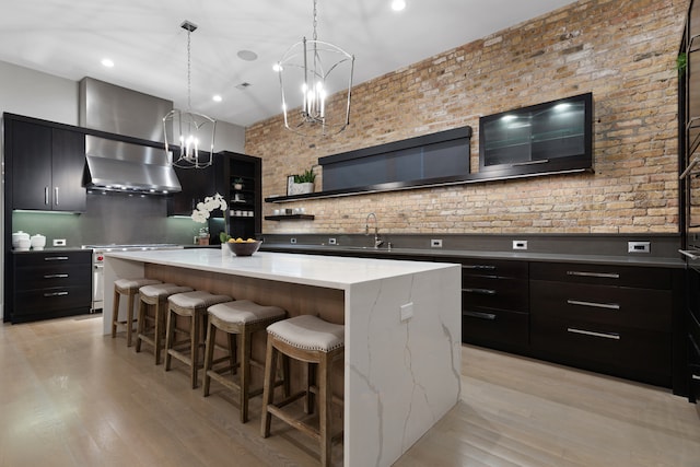 kitchen with light wood-type flooring, a large island, wall chimney range hood, and decorative light fixtures