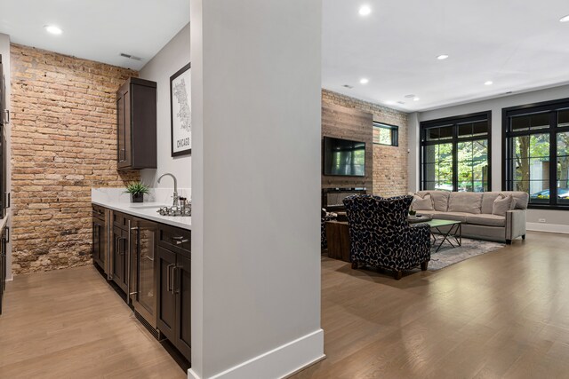 bar featuring light hardwood / wood-style floors, a fireplace, dark brown cabinetry, and sink