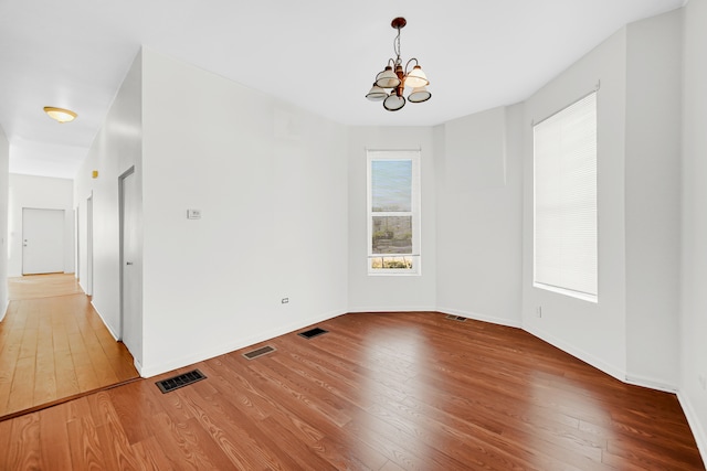 spare room with an inviting chandelier and hardwood / wood-style flooring