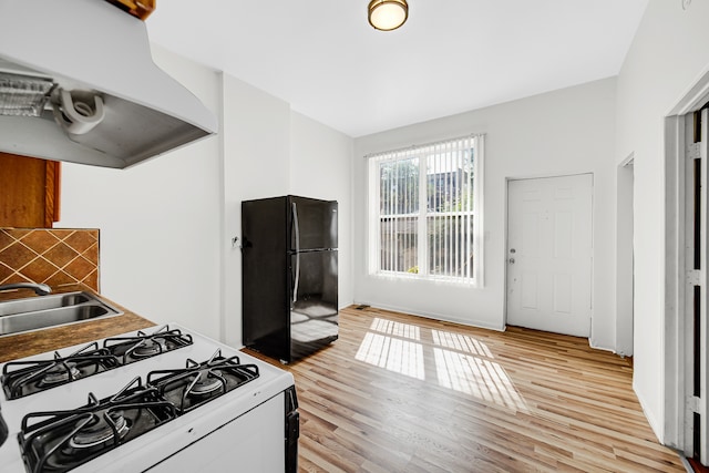 kitchen featuring light hardwood / wood-style floors, black refrigerator, white gas range, and range hood