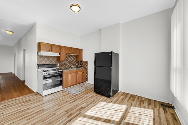 kitchen with decorative backsplash, light wood-type flooring, black refrigerator, and white range with gas stovetop