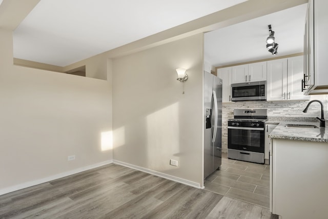 kitchen with light hardwood / wood-style floors, sink, white cabinetry, appliances with stainless steel finishes, and light stone countertops