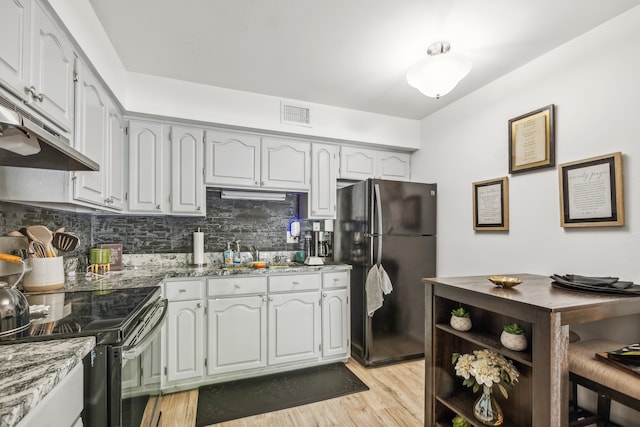 kitchen featuring sink, tasteful backsplash, stainless steel range with electric stovetop, light wood-type flooring, and black refrigerator