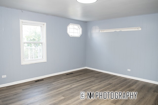 unfurnished room with wood walls and dark wood-type flooring