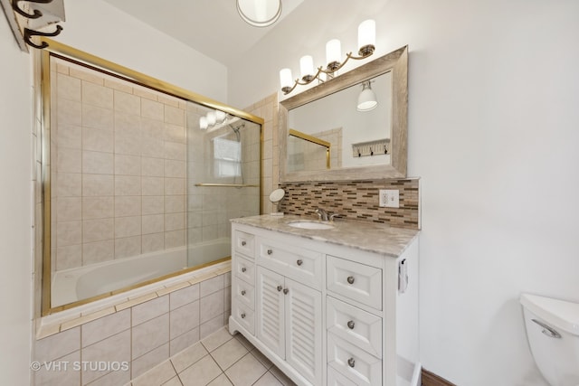 full bathroom featuring vanity, shower / bath combination with glass door, backsplash, tile patterned flooring, and toilet