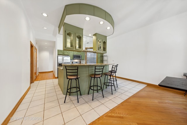 kitchen with green cabinetry, light tile patterned floors, kitchen peninsula, a breakfast bar area, and stainless steel appliances